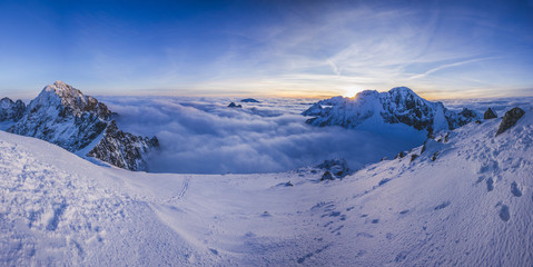 Panorama view of a winter alpine like landscape. Sunset or sunrise in winter snow covered mountains. High alpine summits and peaks in sunset colors of blue, purple and orange. High Tatras, Slovakia.