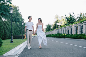 Fototapeta premium bride in wedding dress and groom holding hands and walking on road