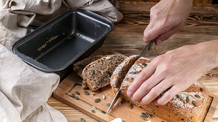 Female hands cut homemade rye bread on a wooden table