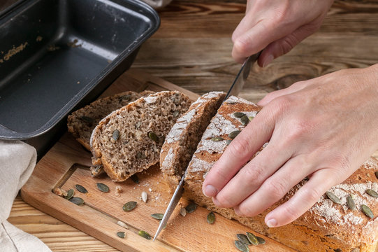 Female hands cut homemade rye bread on a wooden table. Close-Up