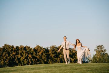 Fototapeta premium beautiful happy young wedding couple running on green meadow in park