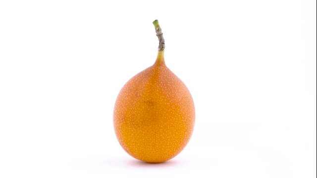 One whole sweet granadilla fruit is rotating on the turntable. Isolated on the white background. Close-up. Macro.
