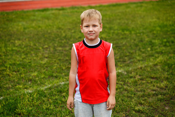 the boy in the red vest standing on green grass