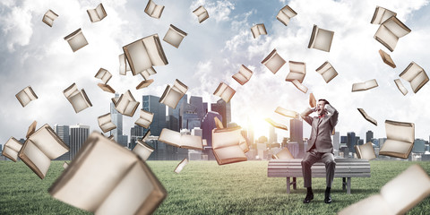 Many old books falling from above and student guy sitting on ben