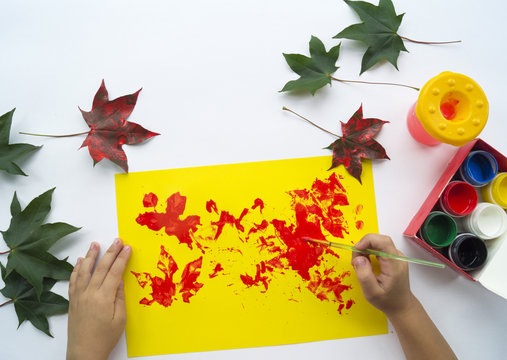 child paints a picture of autumn leaf with paints