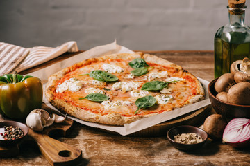 close up view of delicious italian pizza and ingredients on wooden surface
