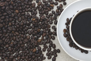 White mug with coffee on a napkin. Spilled coffee beans. Light background, toned photo. Copy space
