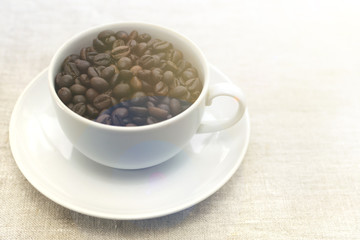 Good morning! Coffee beans in a white cup. Light textured background, toned photo. View from above. Copy space