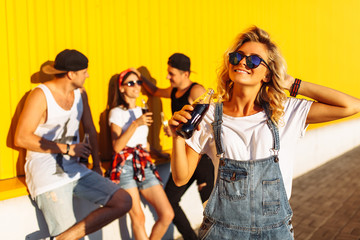 Fototapeta premium portrait of beautiful guys on the background of a group of friends, group of young people with glass bottles with a drink stand near the supermarket, on a yellow background, friends come off in full