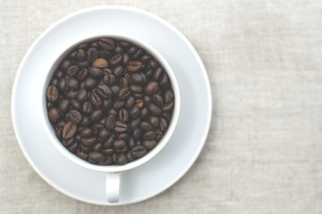 Good morning! Coffee beans in a white coffee cup. Light textured background, toned photo. View from above. Copy space