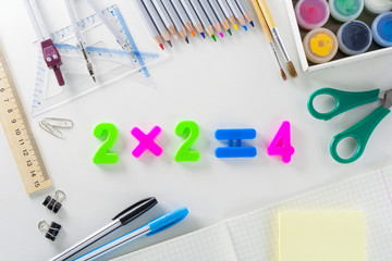 The mathematical equation "2*2=4" from multi-colored plastic numbers on a white background with school articles.