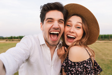 Photo of excited young man and woman dating, and taking selfie together while walking outdoor in countryside