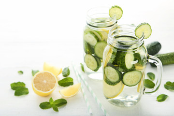 Lemonade with cucumbers, lemons and mint leafs in glass jars on wooden table