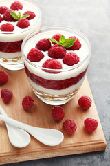 Dessert with raspberries and granola in glasses on grey wooden table