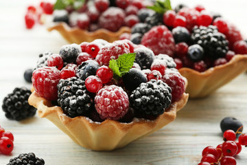Tasty tartlet with berries and powdered sugar on white wooden table