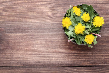 Yellow dandelions in bowl on brown wooden table