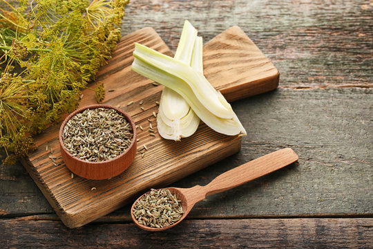 Ripe fennel bulbs and dry seeds in bowl and spoon on wooden table