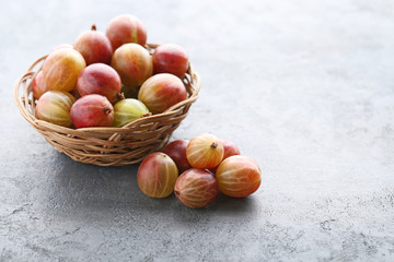 Ripe gooseberries fruit in basket on grey wooden table