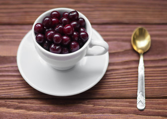 Sweet cherries in a white cup and a teaspoon on a wooden table, selected focus, close up