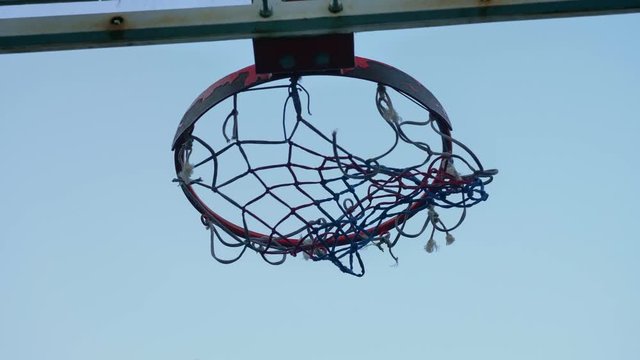 Throwing ball into basketball ring against blue sky, through hoop, outdoors