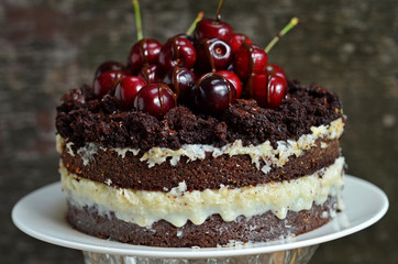 Chocolate cake with coconut cream on a white plate. Cherries on the cake