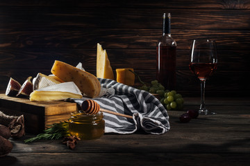 different types of cheeses, honey with stick and wine on table