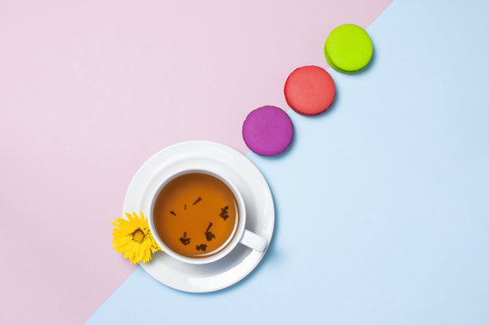 Colorful sweet macaroons, cup of tea and yellow chrysanthemum on pink blue background. Delicious breakfast, beautiful dessert, colorful almond cookies, pastel colors. Top view Flat lay Copy space