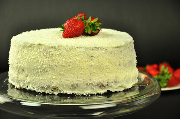 Coconut cake on a glass plateau on a black background. Strawberries on a coconut cake