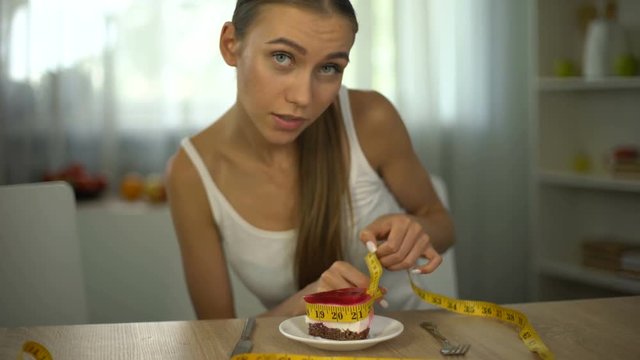 Underweight girl measuring piece of cake with tape, fear of gaining weight