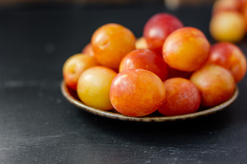 Wild and ripe wild plums on rustic ceramic plate over black background.