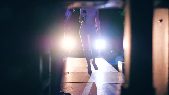 celebrity performs in front of many people in backlight, artist on stage on high-heeled with microphone in evening