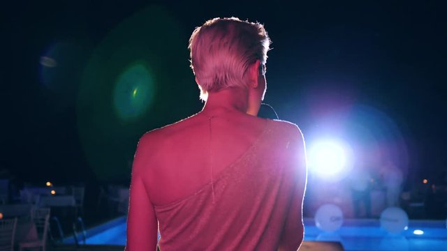 jazz singer with microphone sings in backlight on the summer stage near pool, close up
