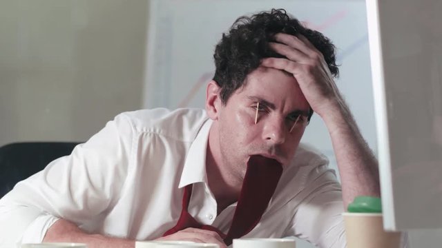 Office worker with matches in eyes drinking a lot of coffee trying not to sleep, eating his tie. Overstrained sleepless marketing manager in office
