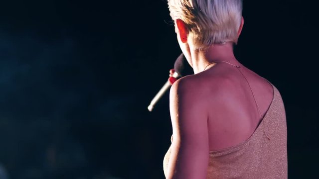 singer sings a song in microphone during performance on stage on concert in backlight