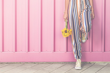 Hipster girl with sunflowers leaning against rose colored wall outdoors.