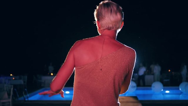 vocalist sings a song with microphone at a nightclub in backlight on the summer stage near pool