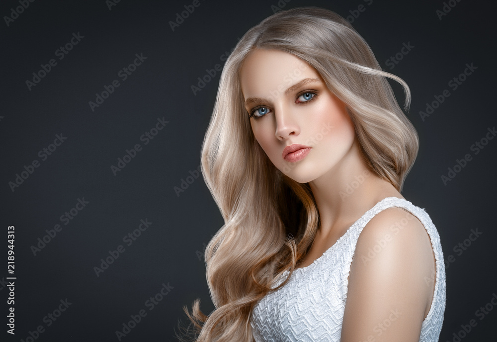 Wall mural Amazing woman portrait. Beautiful girl with long wavy hair. Blonde model with hairstyle over black background