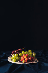 close-up view of various types of grapes on vintage plate on dark fabric on black background