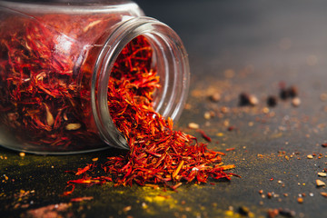 Saffron spice in an open glass jar on dark black background. Seasonings for food. Close-up.
