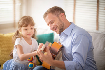 Obraz premium Happy dad and daughter are playing instruments together at home. Dad teach daughter play guitar. Setup studio shooting. Selective focus at father's face.