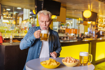 Favourite drink. Nice pleasant man holding a glass with beer while being in the sports club