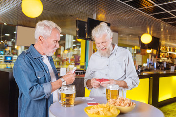 Old gamblers. Joyful happy men playing cards while meeting in the pub