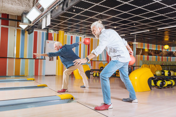 Bowling tournament. Delighted positive men playing together while participating in the bowling tournament