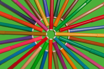 new bright plastic colored felt pens forming a circle lying on a green surface. concept of office supplies