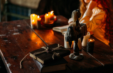 on the old vintage wooden table is a candlestick with candles. A red-haired girl in vintage clothes is sitting at the table, reading a book old book on a wooden table by candlelight