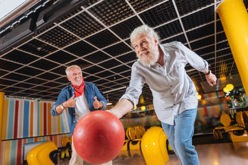Great throw. Cheerful positive man smiling while throwing the bowling ball - obrazy, fototapety, plakaty