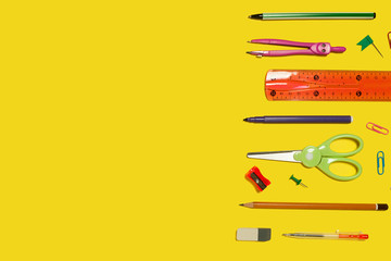 row of different school and office stationary and gadgets lying on a yellow background. free space...