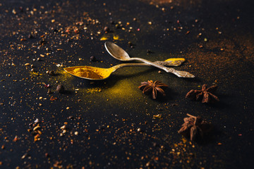 Assorted spices in spoons with empty space for text on dark black background. Seasonings for food. Curry, paprika, pepper, cardamom, anise, cloves, turmeric. Close-up.