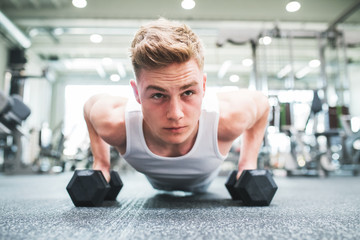 Obraz na płótnie Canvas A close-up of young fit man in gym doing push ups on dumbbells.