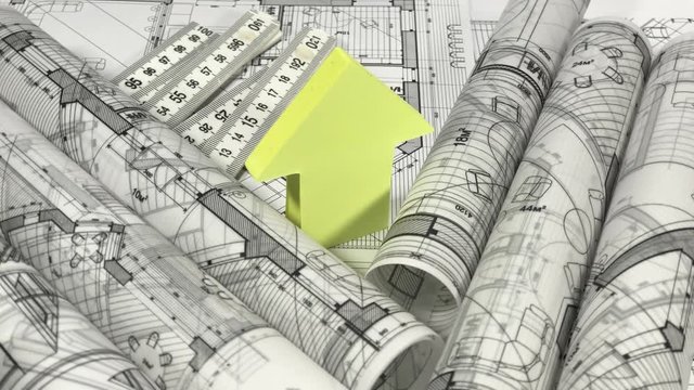 Blueprints - rolls of architectural drawings, yardstick - folding ruler and house symbol from a pack of yellow stickers smoothly rotate on the surface of the architectural drawings